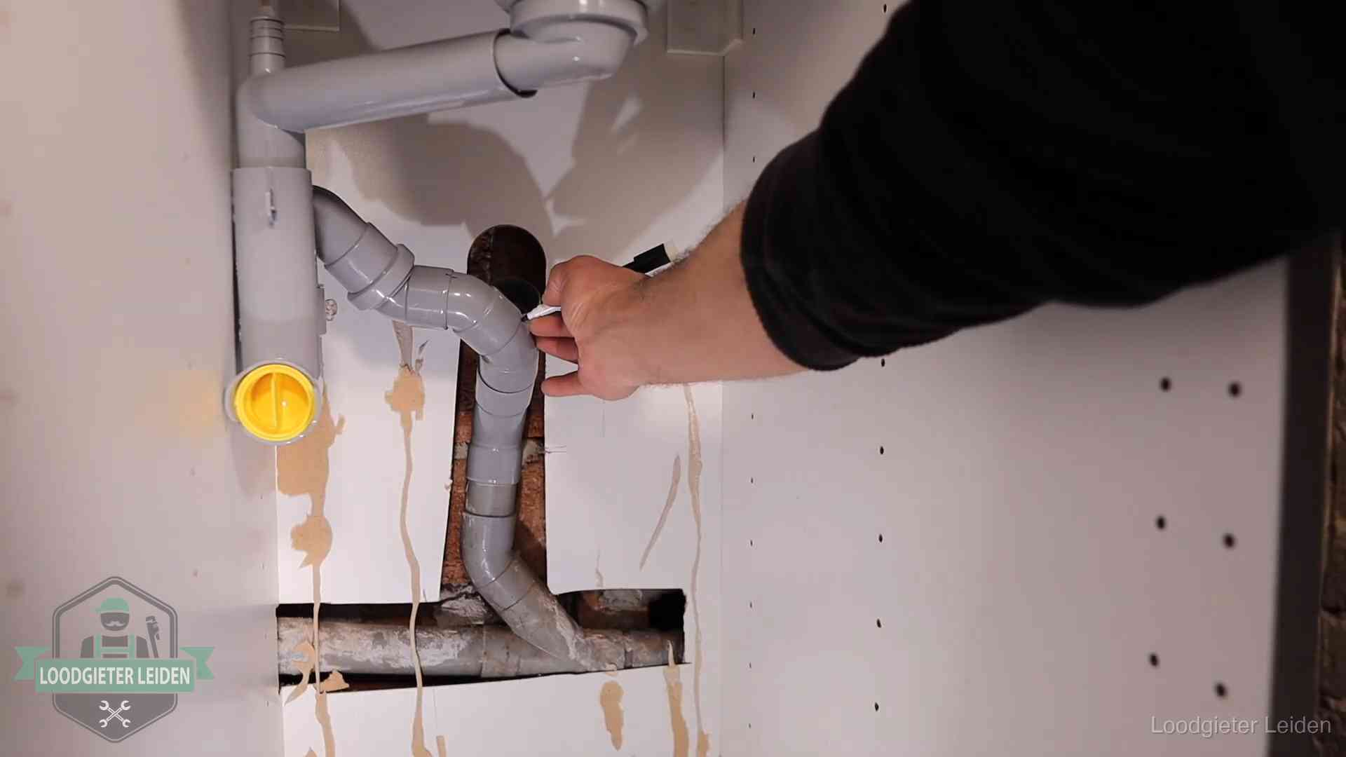 Loodgieter voor verhuurders en bedrijven in Leiden Loodgieter markeert een pvc-afvoerbuis onder een gootsteen in Leiden