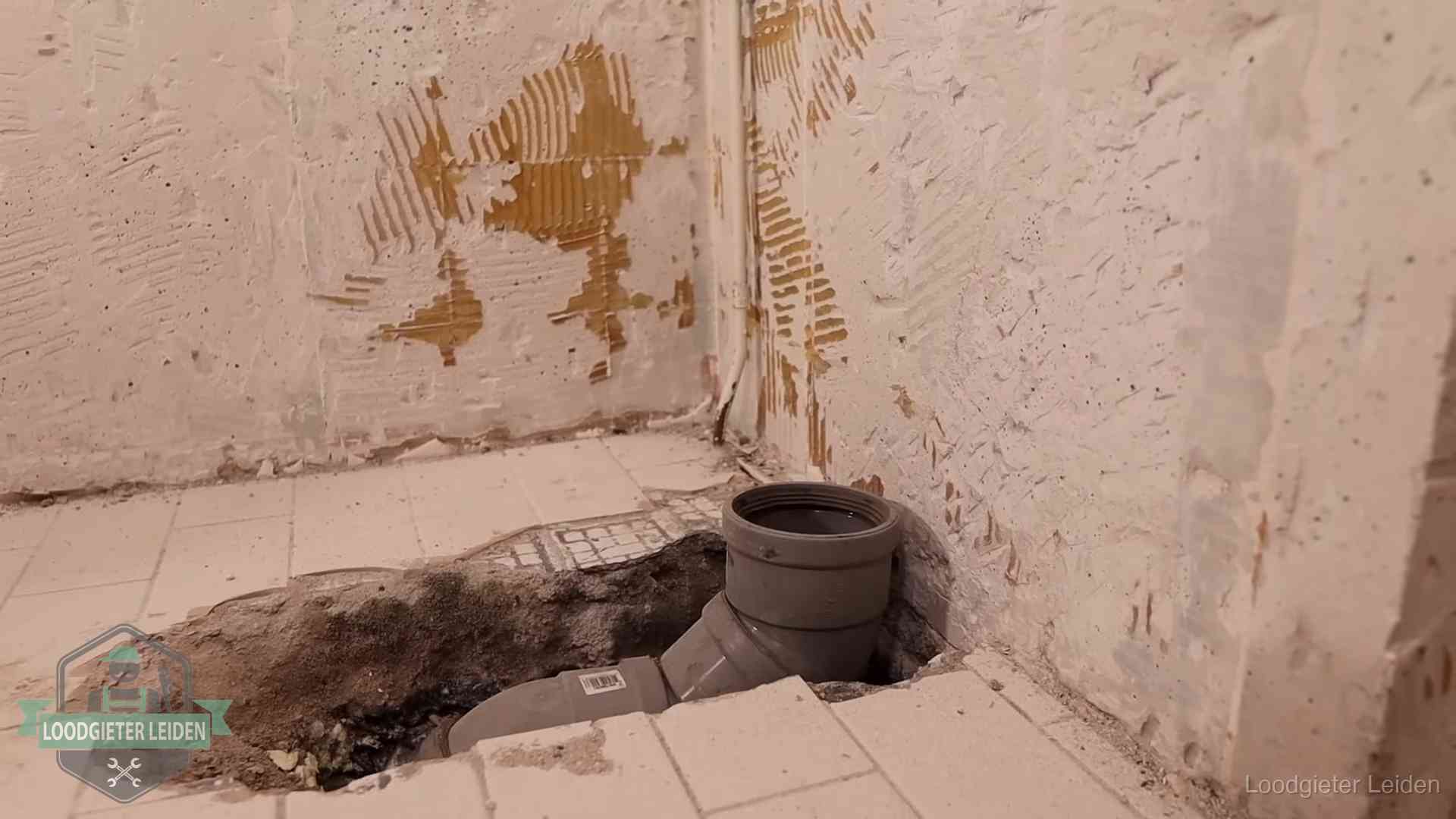 Verzakt riool herstellen in Leiden Opengebroken vloer met een nieuwe pvc-rioolbocht in een gegraven sleuf in Leiden