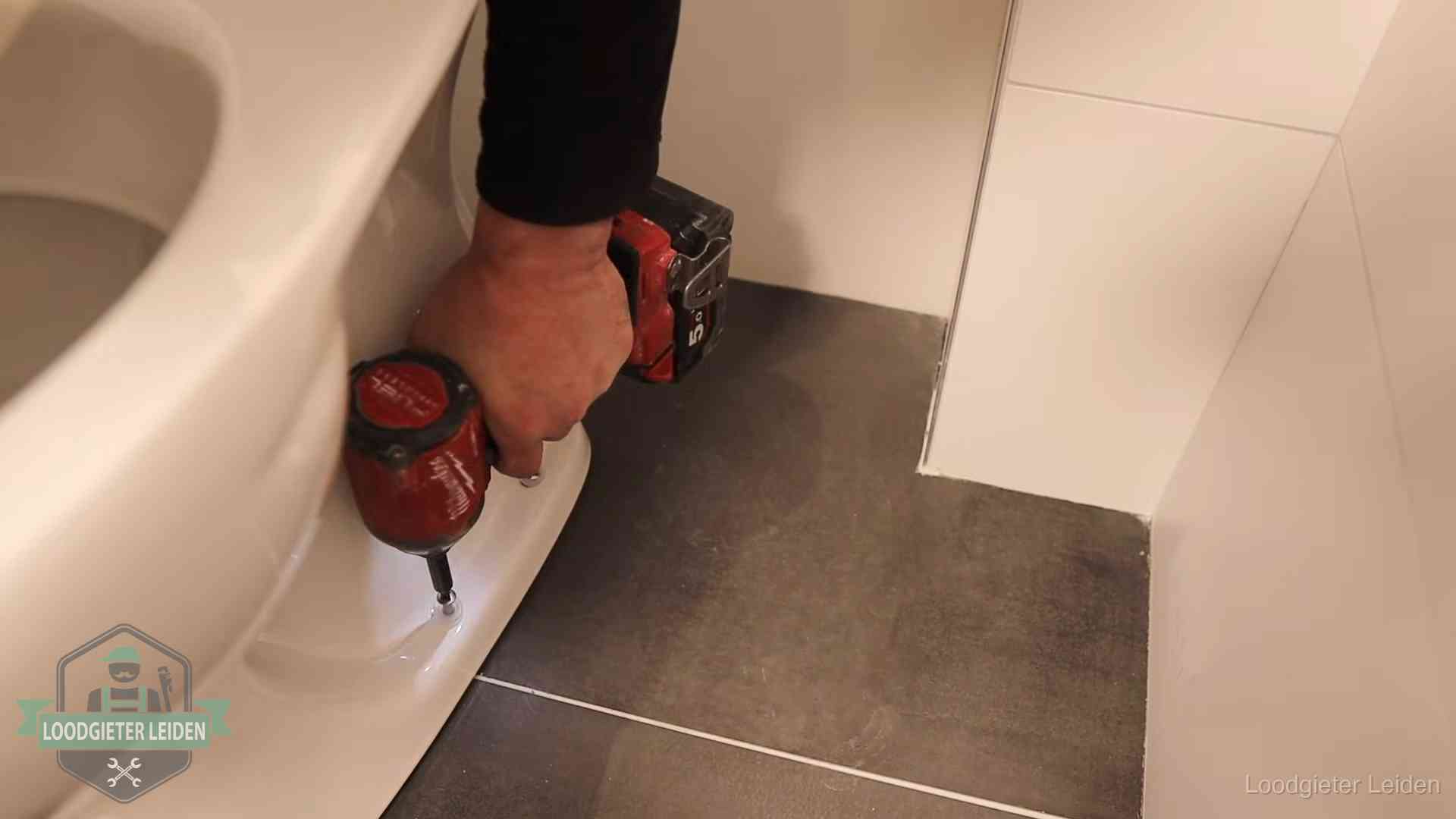 Kosten wc ontstoppen in Leiden Loodgieter zet de voet van een wc-pot vast op de tegelvloer in Leiden